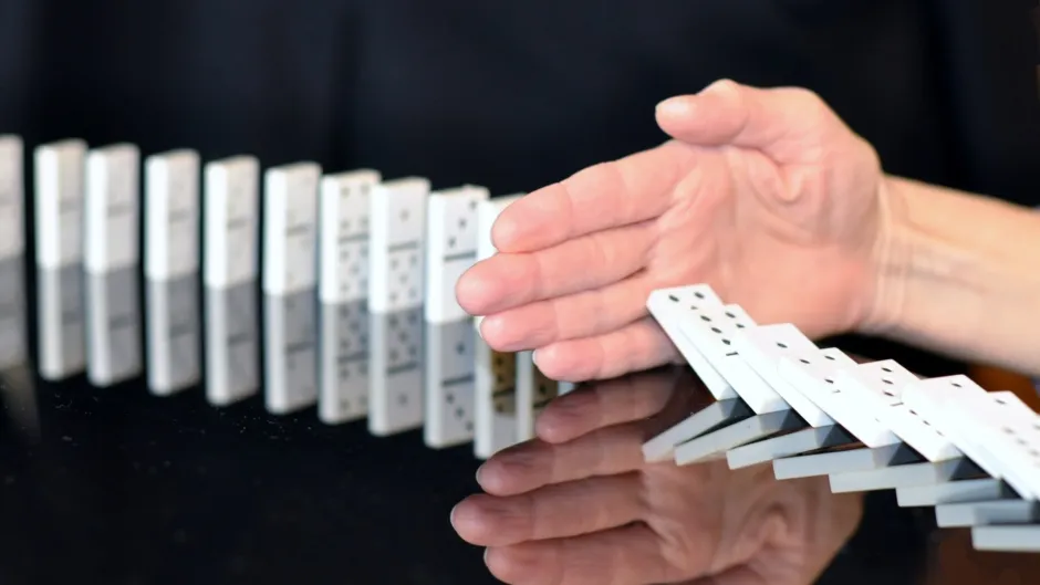 Hand hält umfallende Dominosteine auf